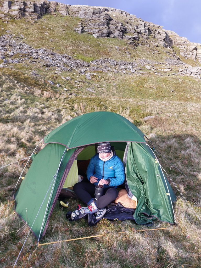 A technical backpacking tent pitched securely on a dry, sheltered grassy ledge on Moel Ysgyfarnogod.