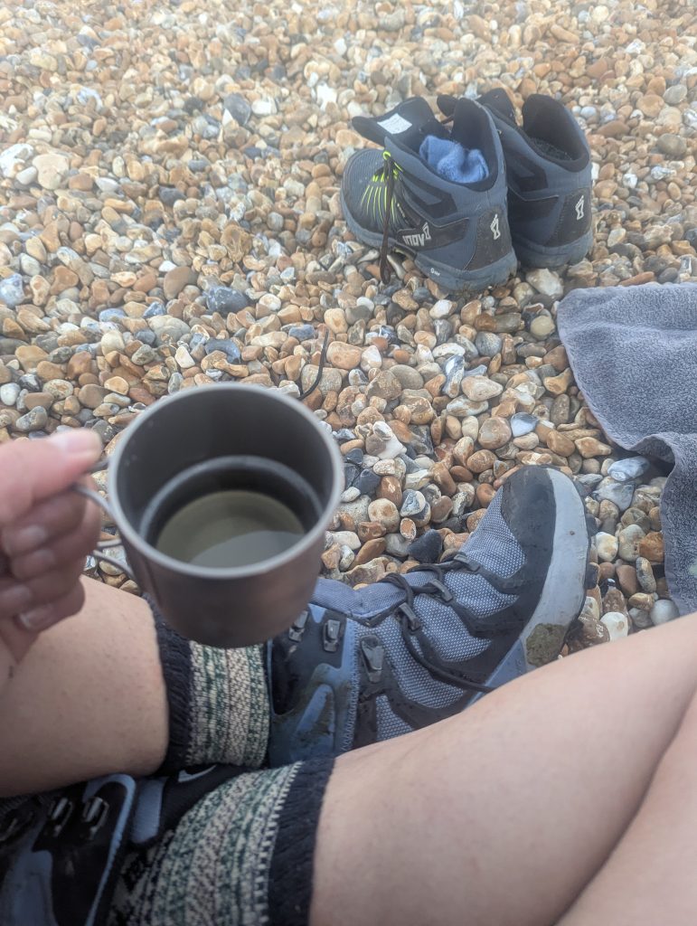 Two rugged titanium camping mugs filled with celebratory sparkling prosecco on a pebble beach.