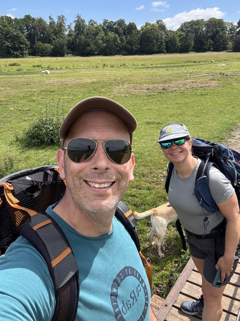 Two happy hikers taking a quick selfie while walking along a sunny path in the Kent Downs.