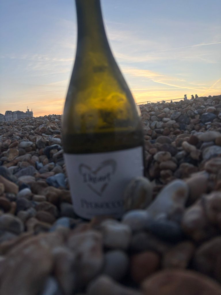 A glowing, golden sunset reflecting over the ocean waves with a bottle of prosecco resting on the pebbles.