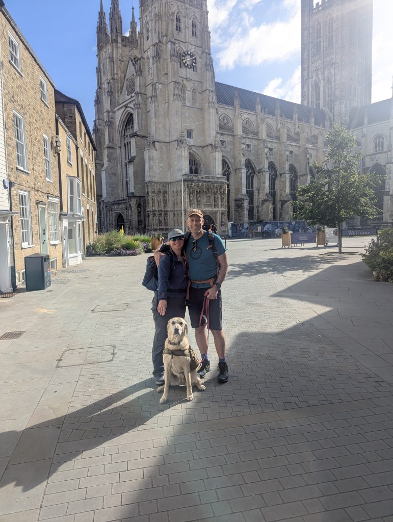 Trail dog Poppy and hikers standing in front of the historic Canterbury Cathedral at the start of the Elham Valley Way.