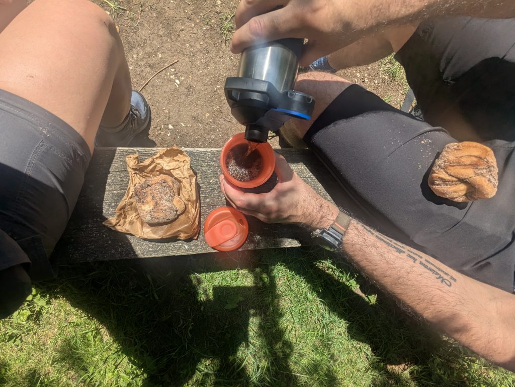 Sweet cinnamon buns and a thermos of hot coffee resting on a wooden bench outdoors.