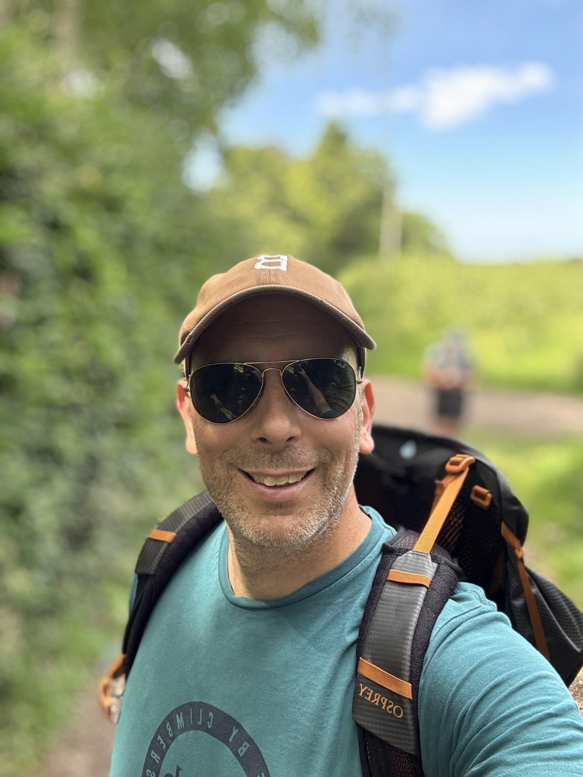 Former Royal Marine and Trail Dog author Terry wearing a blue technical outdoor jacket and backpacking rucksack, standing on an exposed mountain trail looking out over open ridge terrain.