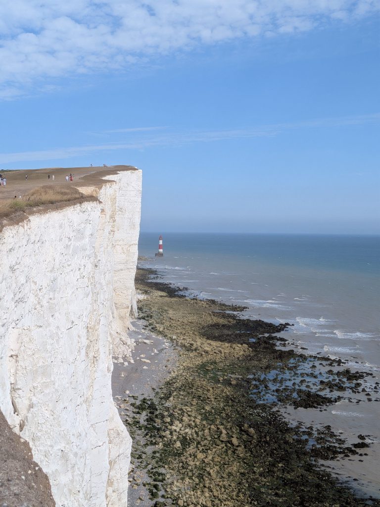 Sheer 160-meter white chalk cliff face at Beachy Head dropping into the rocky seabed with the iconic red-and-white striped lighthouse standing below.