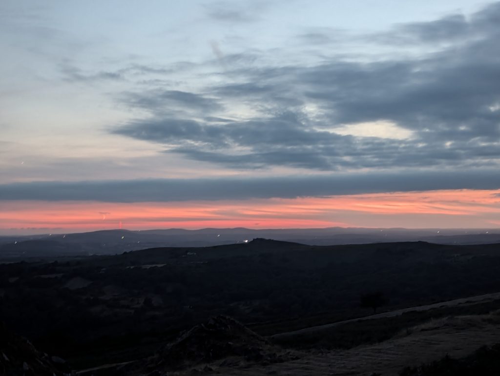 Deep red and orange sky glow along the dark silhouette of Dartmoor hills at twilight after sunset.
