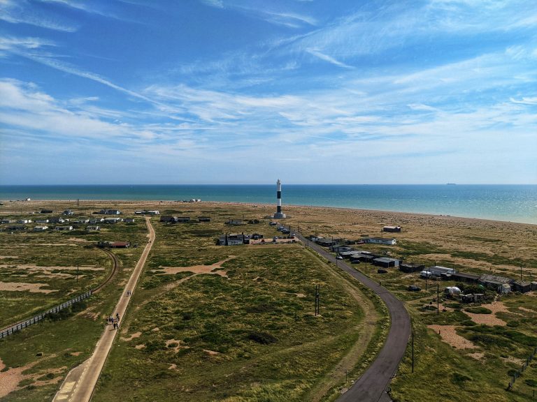 Elevated panoramic view of the modern black and white Dungeness lighthouse and the English Channel.