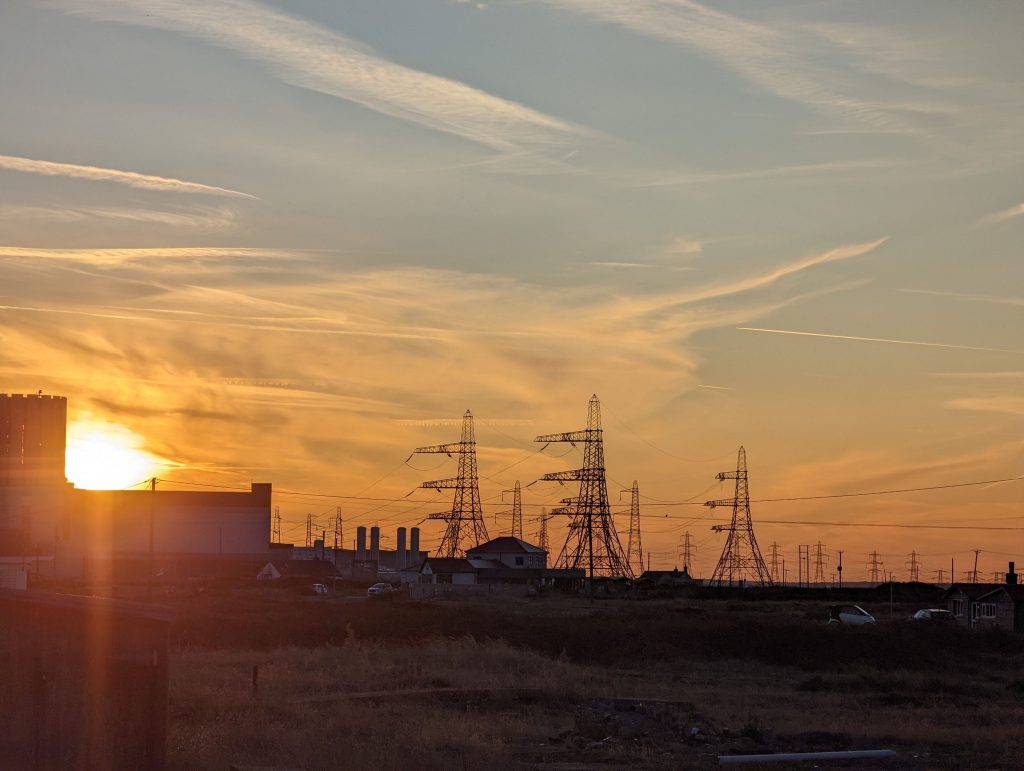 Golden sunset dropping behind the massive concrete blocks and complex electrical pylons of the Dungeness B Nuclear Power Station.