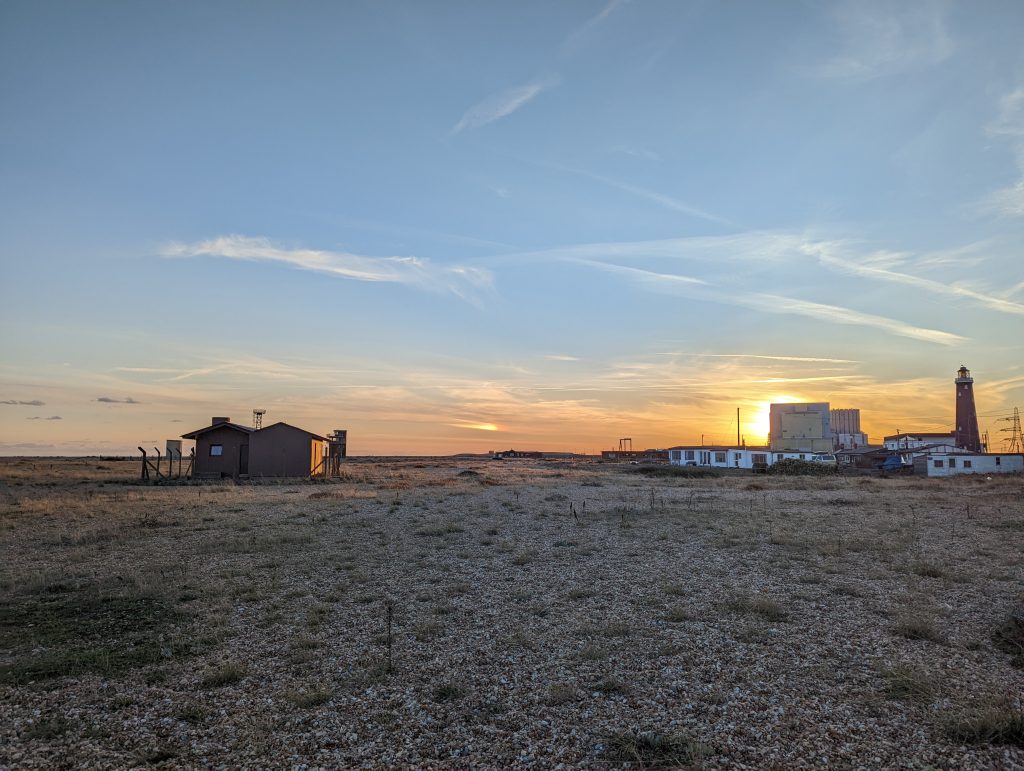 Golden hour sunset dropping behind the Dungeness power station and Old Lighthouse across the shingle desert.