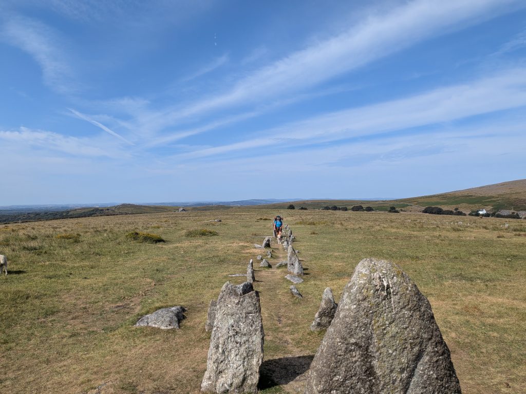Backpacker and dog walking between the parallel granite double stone rows at Merrivale Prehistoric Settlement.