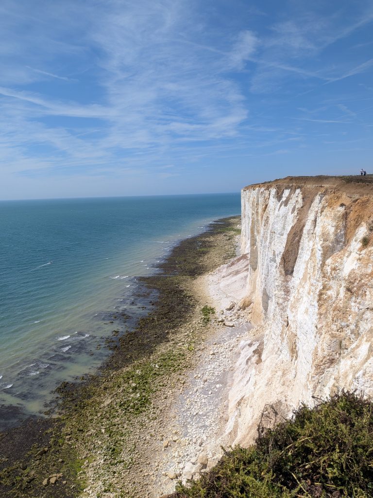 Looking along the edge of towering, sheer white chalk cliffs dropping vertically into the turquoise sea along the South Downs coast.