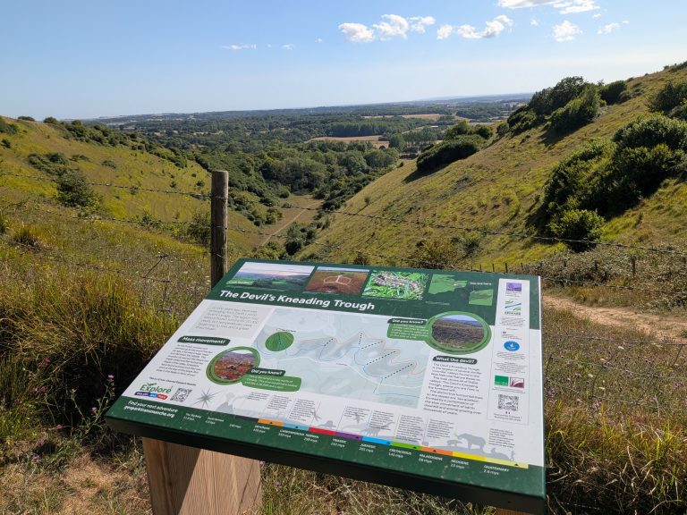 Wooden information board for The Devil's Kneading Trough overlooking the steep, green, v-shaped valley in the Kent Downs AONB.