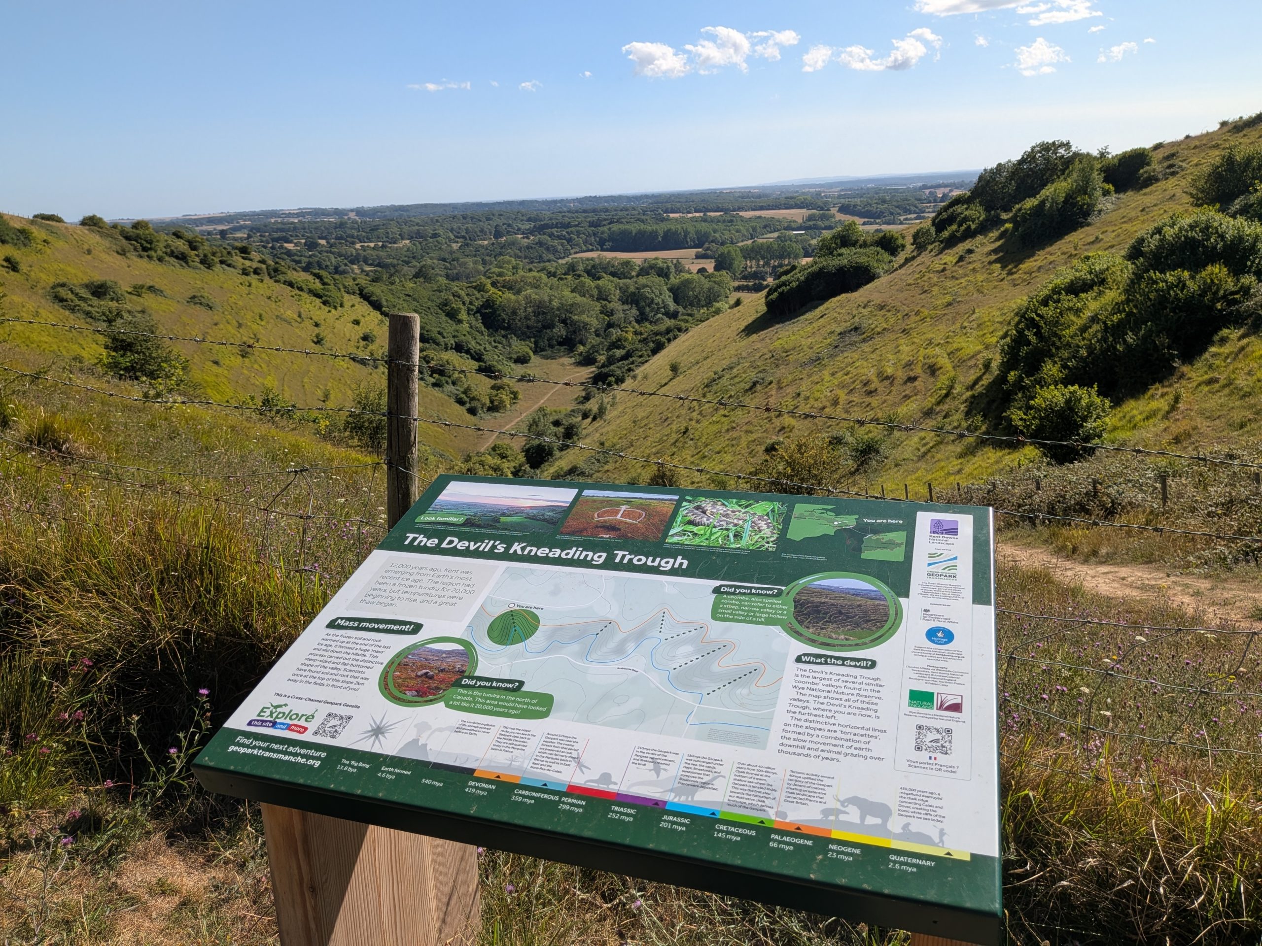 Wooden information board for The Devil's Kneading Trough overlooking the steep, green, v-shaped valley in the Kent Downs AONB.