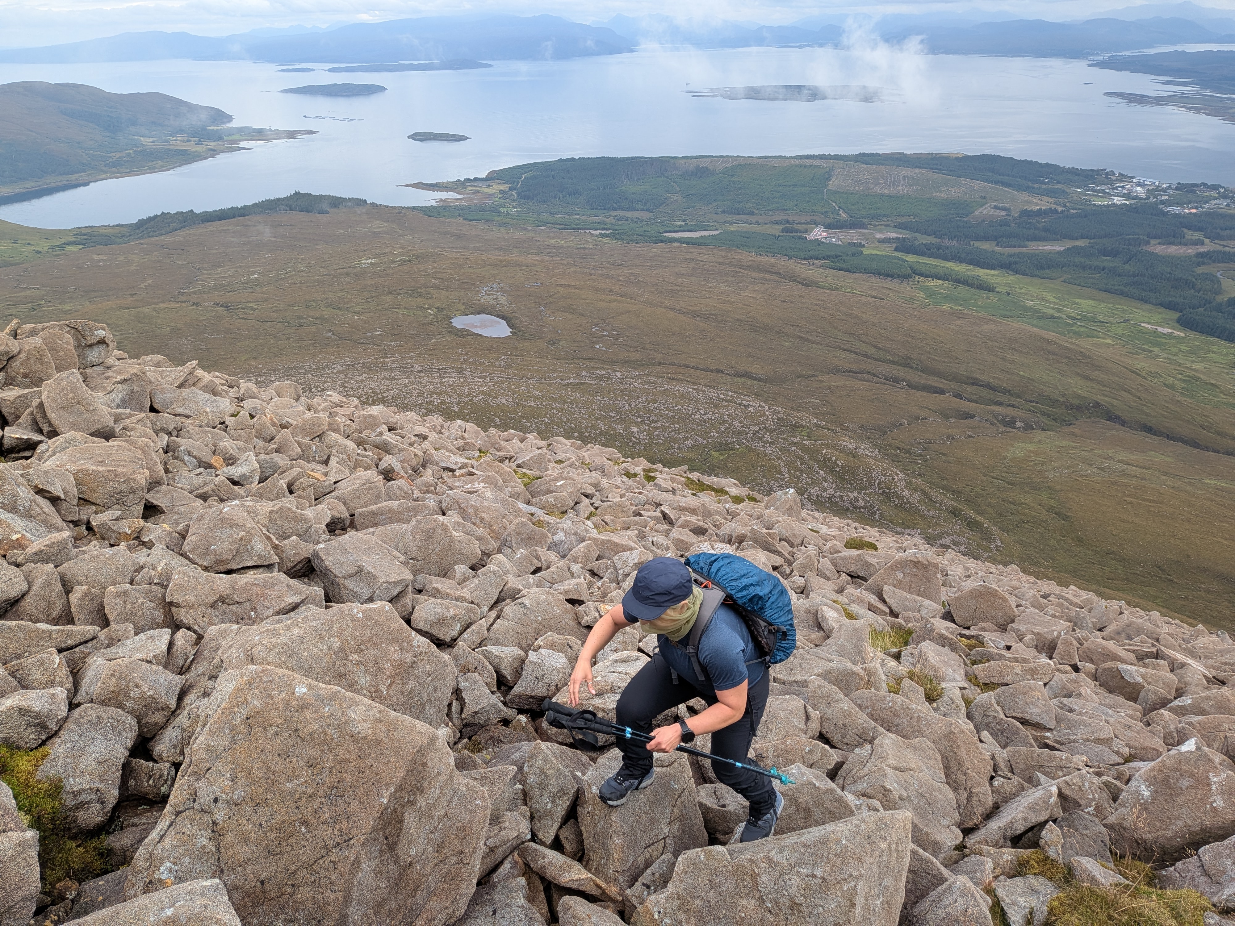 Hiker wearing Inov-8 Roclite Pro Mid boots climbing steep rocky ridge on Beinn na Caillich overlooking ocean lochs on Skye.