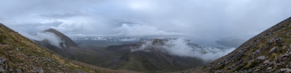 Panoramic view of dramatic mountain peaks and valleys with thick cloud banks clinging to the high slopes.