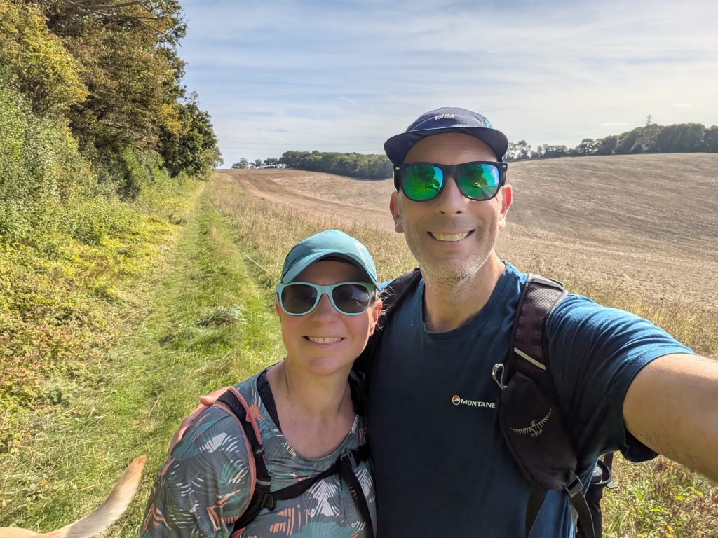 Smiling male and female hikers wearing caps and sunglasses taking a selfie on a sunny countryside field path
