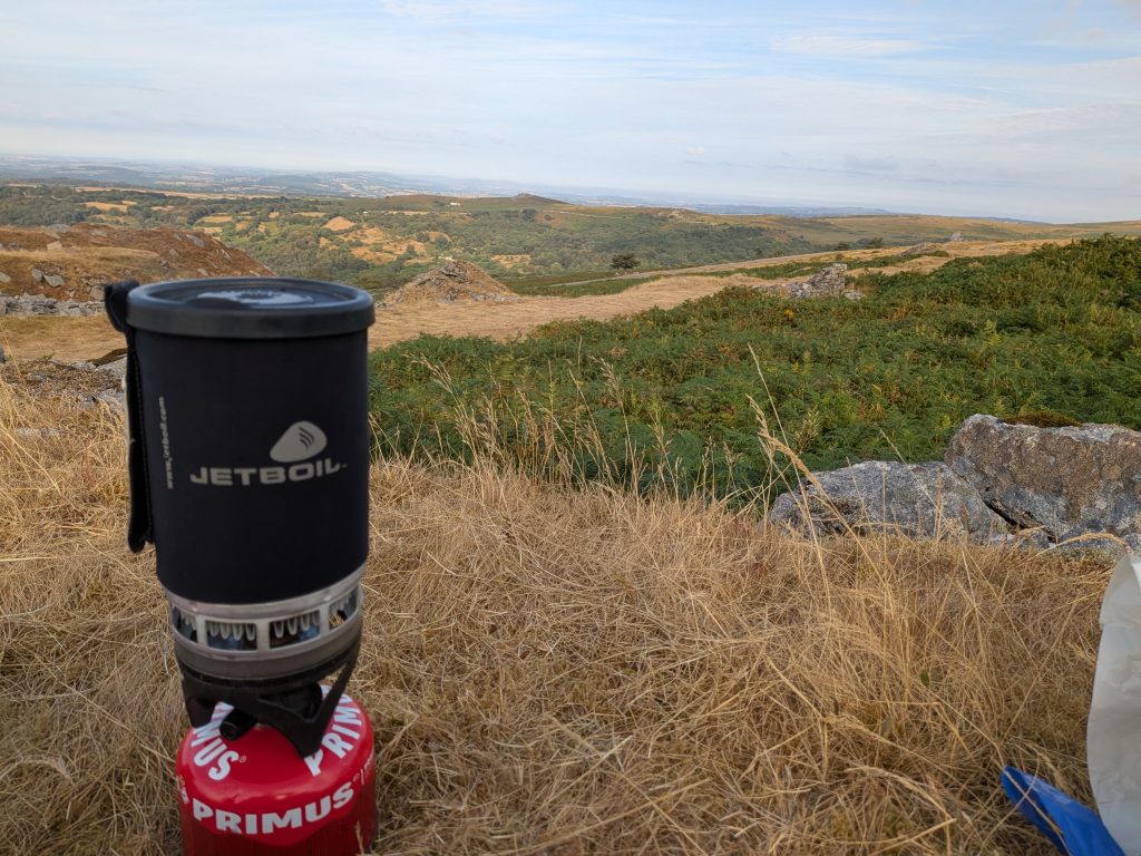 Original 2006 Jetboil PCS attached to a red Primus power gas canister sitting in dry brown tussock grass on a high UK moorland ridge.