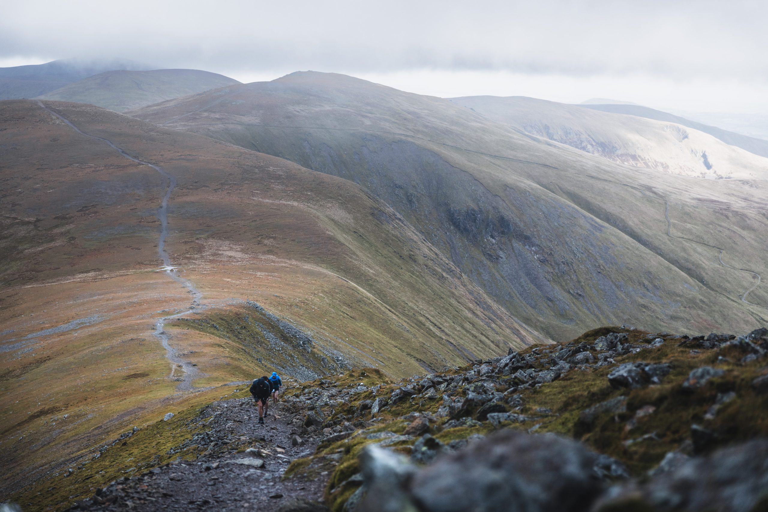 Trail runners navigating a long, winding mountain path along an exposed ridge during the Lake District ultra.