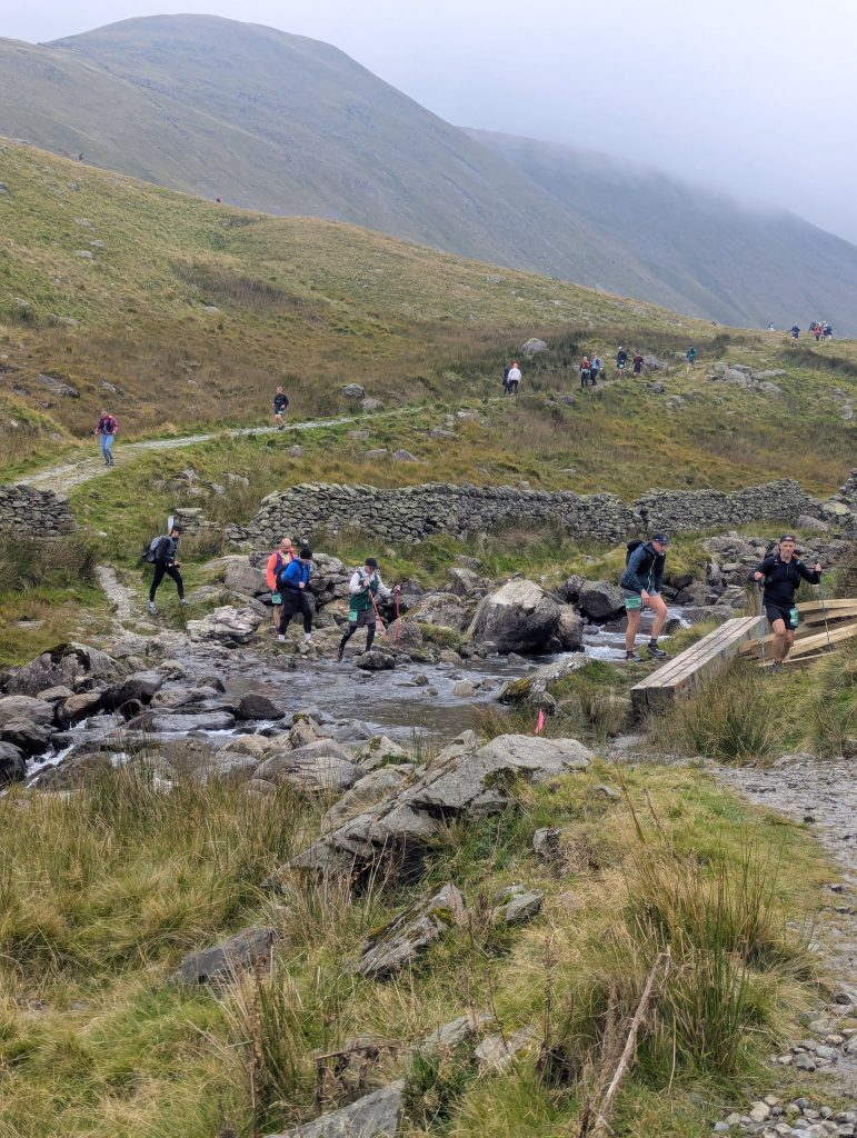 Trail runners wading across the rocky River Caldew during a Lake District ultra marathon.