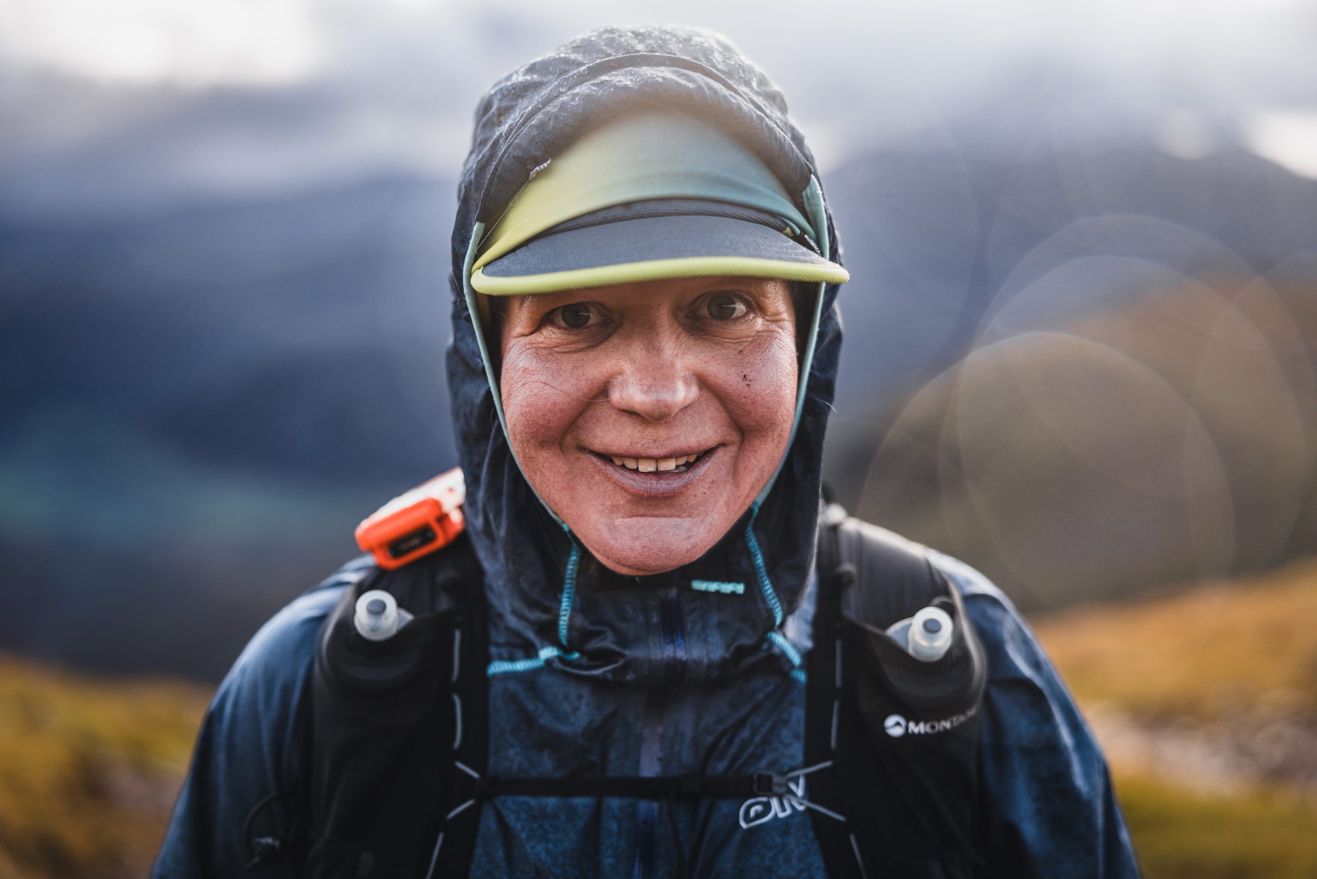 Close-up portrait of a smiling ultra runner weathering the elements in a technical waterproof jacket and cap in the fells.