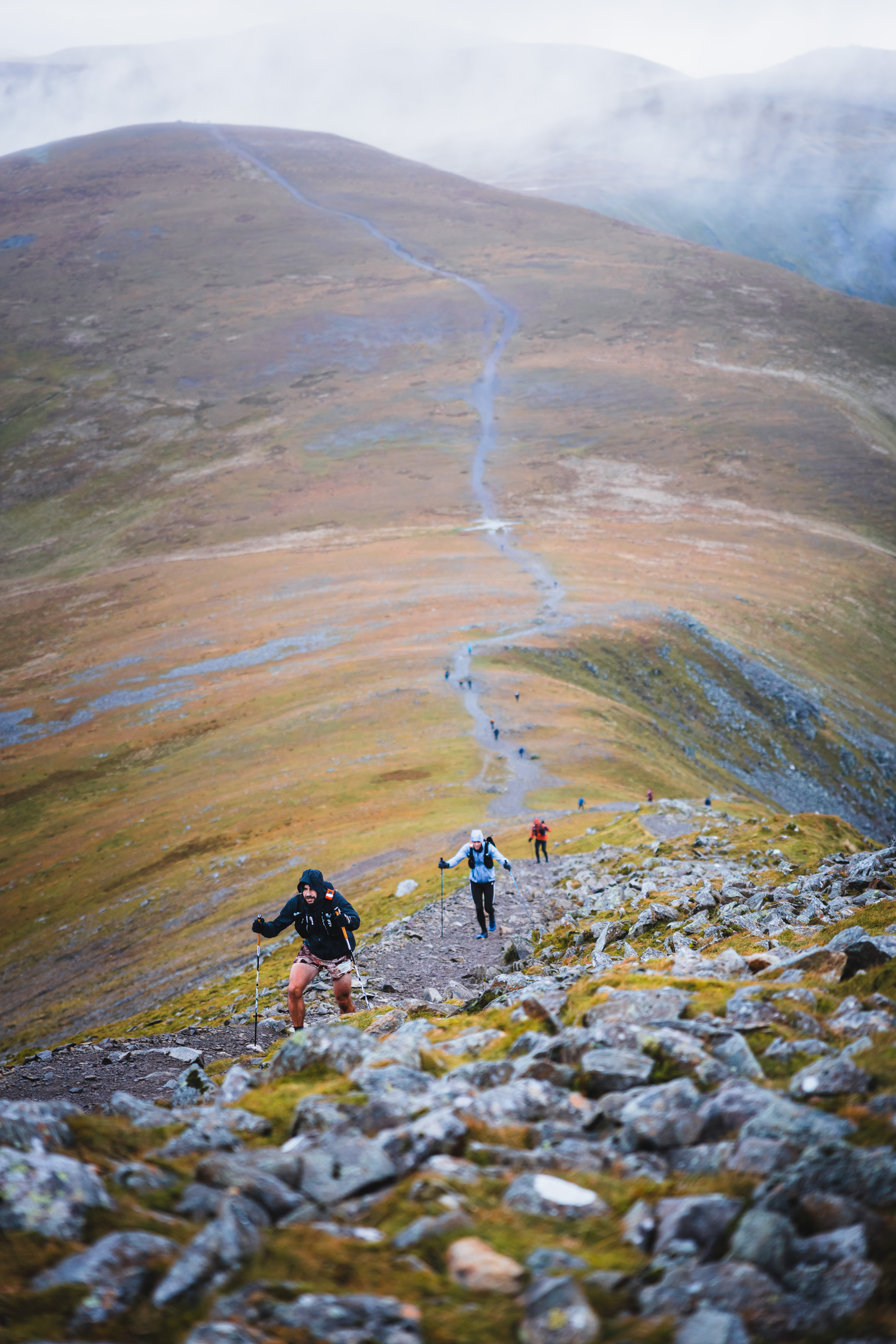 Ultra runners using trekking poles to climb a steep, rocky mountain incline on the course.