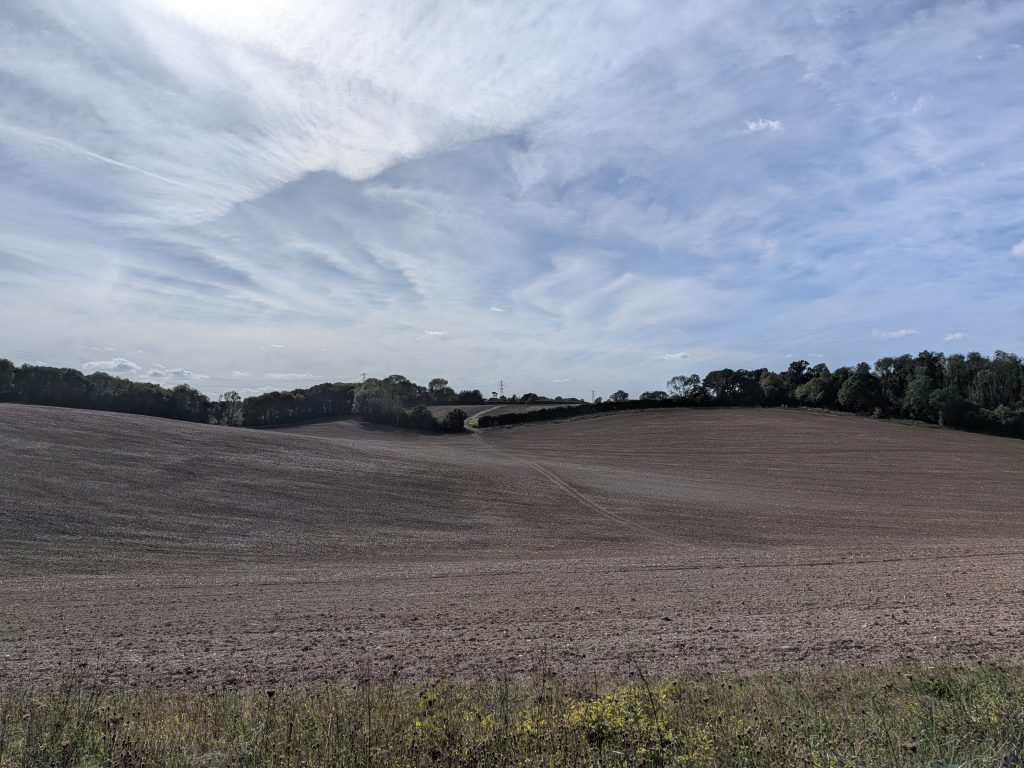 Wide panoramic view of undulating ploughed fields and chalk valleys in the Kent Downs under a cloudy sky