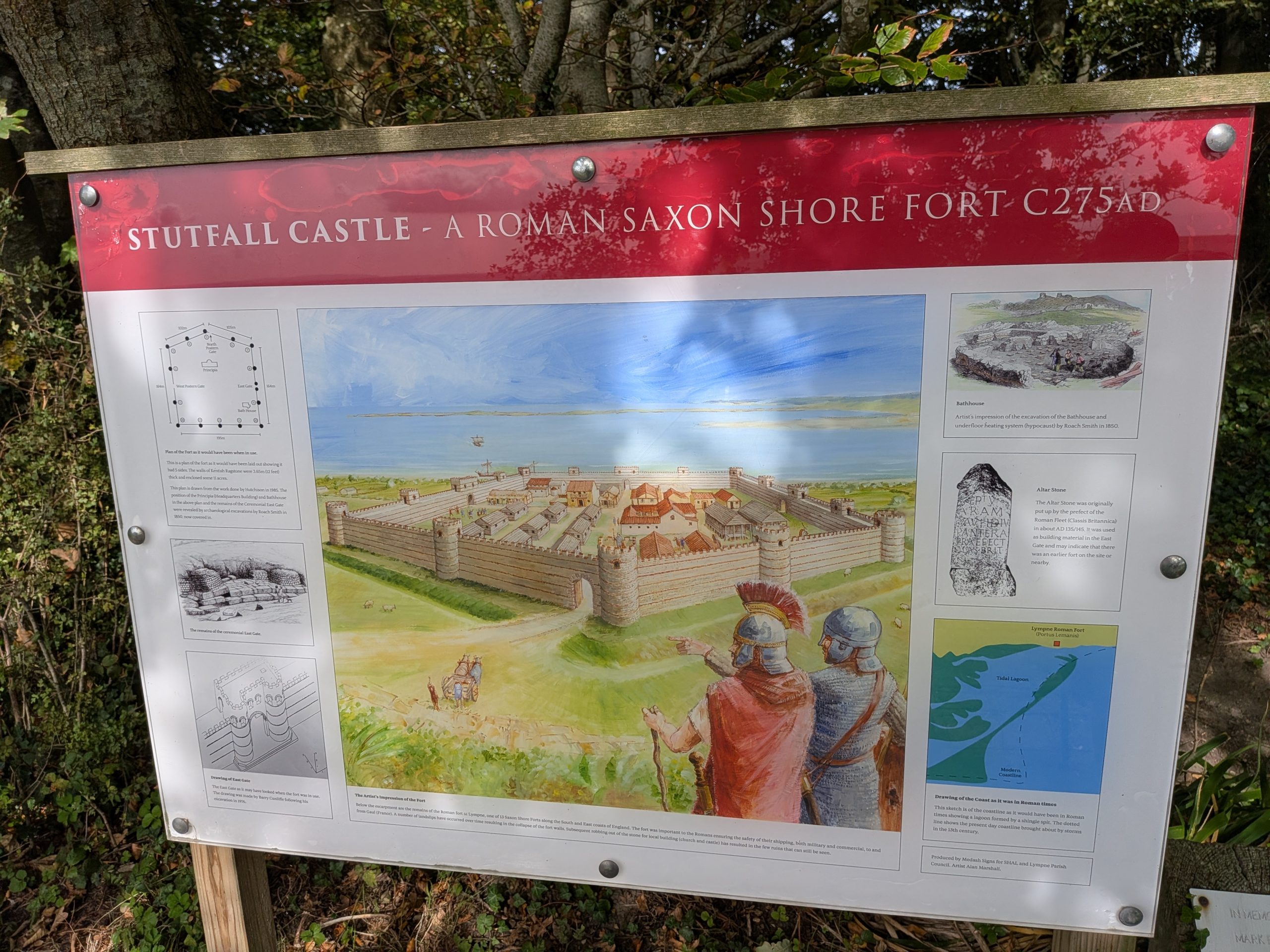 A red and white heritage information board detailing the history and layout of Stutfall Castle, a Roman Saxon Shore Fort from around 275 AD, featuring an artist's impression of the walled settlement.
